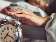 man in bed snoozing an alarm to get more sleep during daylight savings time