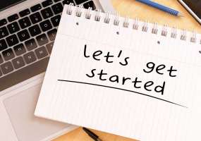 Picture of a Notebook that says "Let's Get Started" by a computer